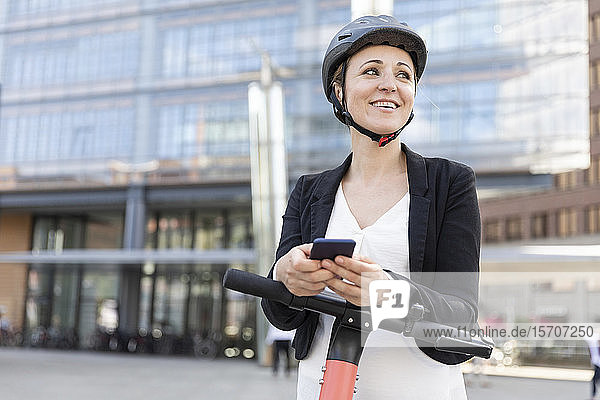 Happy woman with e-scooter and smartphone in the city  Berlin  Germany