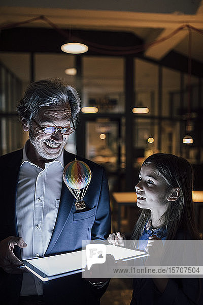 Happy senior buisinessman and girl with hot-air balloon and shining tablet in office
