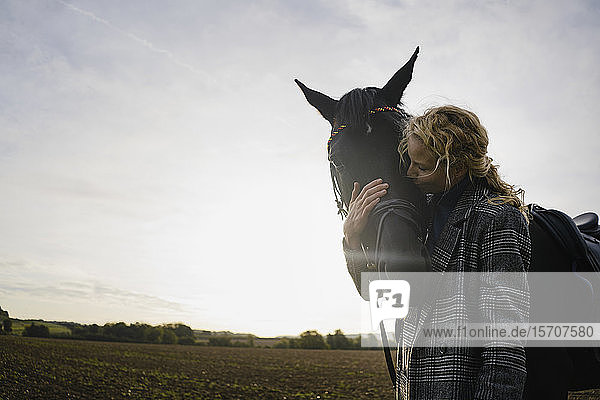 Liebevolle junge Frau mit Pferd auf einem Feld auf dem Land bei Sonnenuntergang