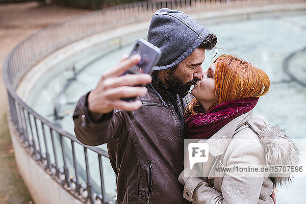 Kissing couple taking selfie with smartphone