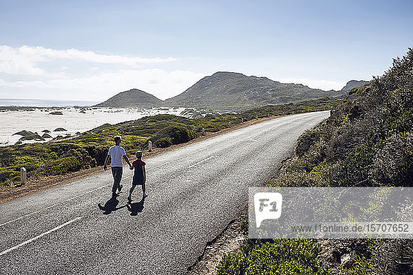 Mann geht Hand in Hand mit seiner Tochter auf der Landstraße  Kapstadt  Westkap  Südafrika