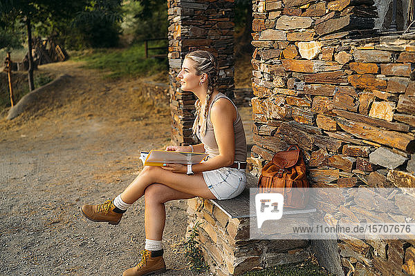 Frau mit Ordner sitzt an einem Steinhaus auf dem Land
