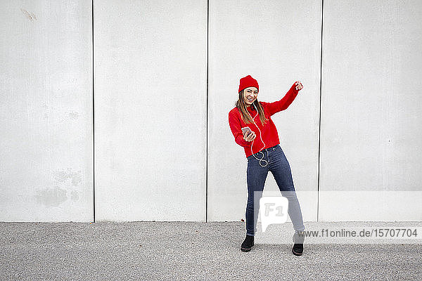 Woman wearing red pullover and wolly hat and dancing in front of a wall