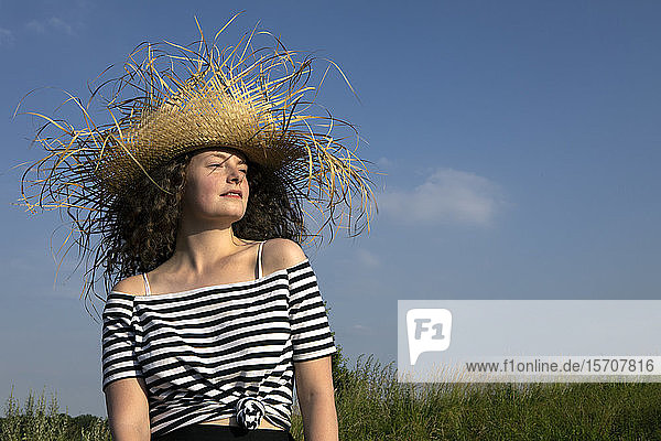 Porträt einer jungen Frau mit ausgefranstem Strohhut in der Natur