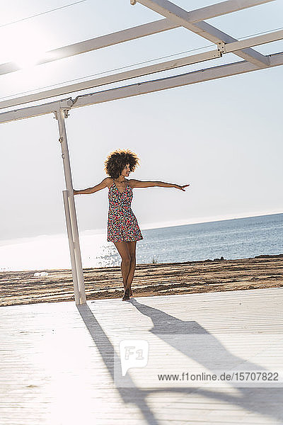 Junge Frau im Sommerkleid genießt das Sonnenlicht auf einer Terrasse am Strand
