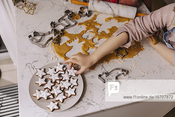 Nahaufnahme eines Mädchens das Weihnachtsplätzchen vom Teller auf dem Küchentisch nimmt