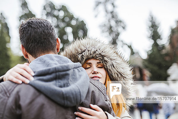 Porträt einer jungen Frau mit geschlossenen Augen  die ihren Freund im Freien umarmt