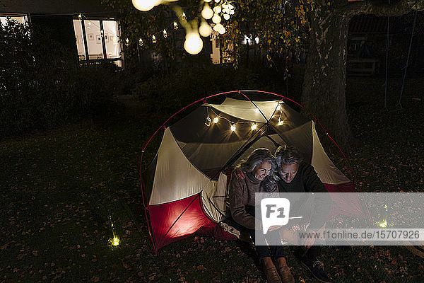 Älteres Ehepaar mit Tablette zeltet nachts im Garten seines Hauses