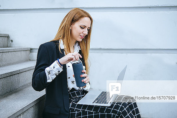 Junge Geschäftsfrau sitzt auf einer Treppe mit Laptop und wiederverwendbarer Flasche