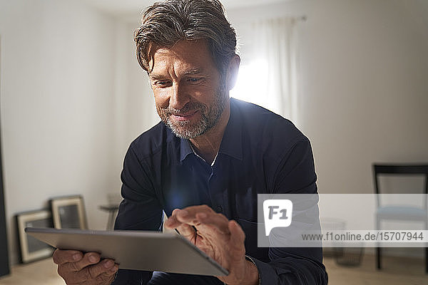 Porträt eines lächelnden  reifen Mannes  der zu Hause ein digitales Tablet benutzt