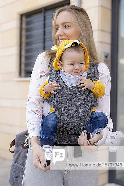 Happy mother carrying baby boy in a sling outdoors