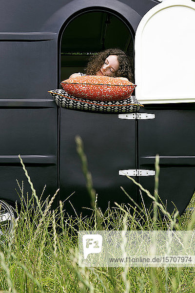 Junge Frau in einem Wohnwagen  die sich auf Kissen stützt und sich ausruht