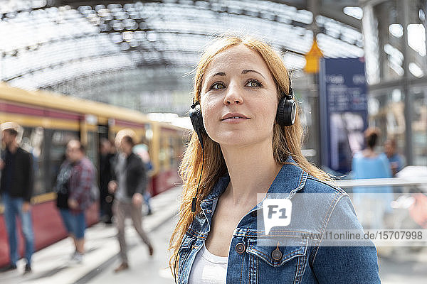 Porträt einer Frau  die am Bahnhof mit Kopfhörern Musik hört  Berlin  Deutschland