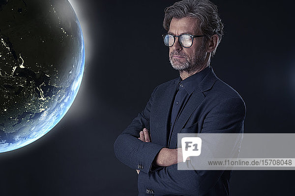 Porträt eines reifen Geschäftsmannes vor dunklem Hintergrund beim Beobachten des schwebenden Planeten Erde