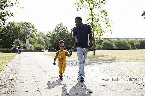 Father and daughter walking hand in hand on a path in a park