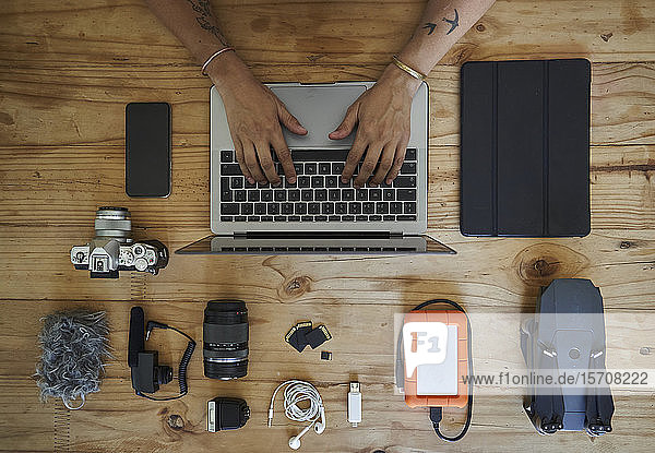 Person sitting at table with photografic equipment using laptop overhead view
