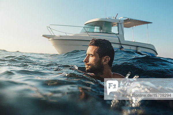 Junger Mann schwimmt im Meer vor der Yacht