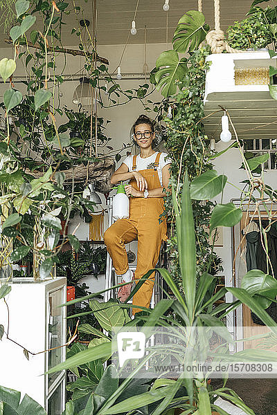 Porträt einer jungen Frau  die auf einer Leiter in einem kleinen Gartenbaubetrieb steht