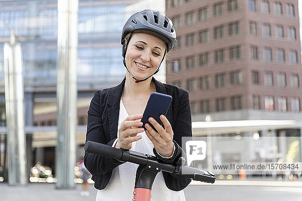 Frau mit E-Scooter mit Smartphone in der Stadt  Berlin  Deutschland