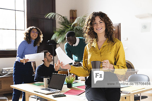 Porträt einer lächelnden Frau im Büro mit Kollegen im Hintergrund