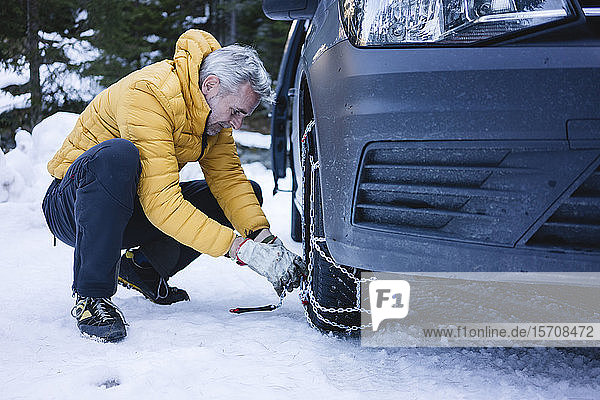 Mann legt die Schneeketten an sein Auto