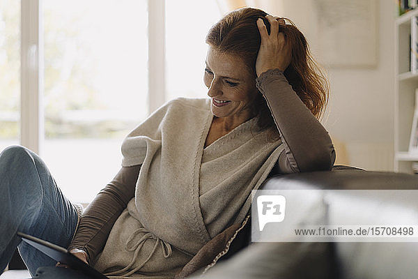 Lächelnde Frau sitzt auf dem Sofa und benutzt ein digitales Tablett