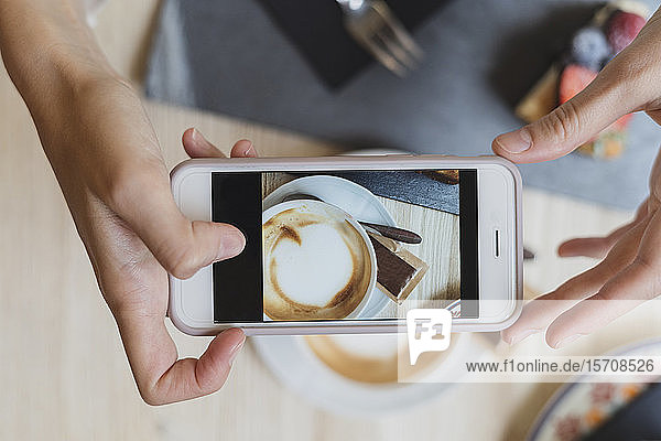 Draufsicht einer Frau in einem Cafe  die ein Handyfoto von Cappuccino macht