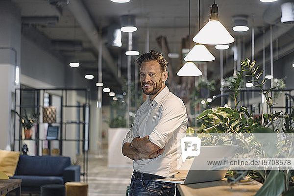 Portrait of smiling mature businessman with laptop in modern office lounge
