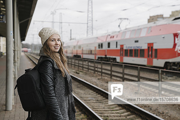 Porträt einer lächelnden jungen Frau mit Rucksack auf dem Bahnsteig wartend  Vilnius  Litauen