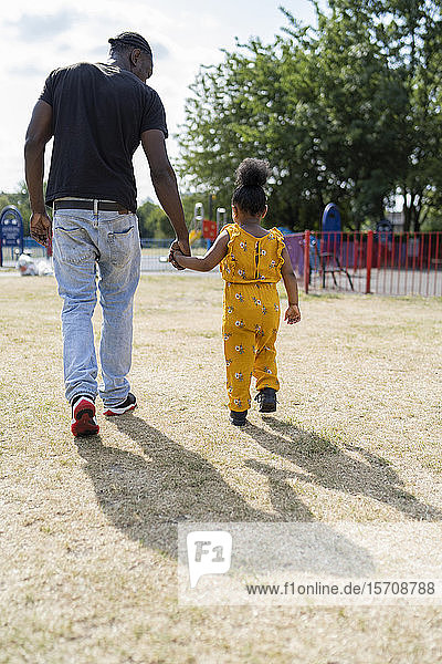 Rear view of father and daughter walking hand in hand in a park