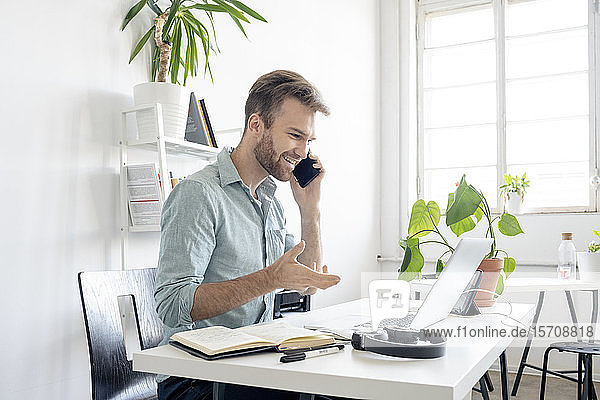 Lächelnder Mann am Telefon am Schreibtisch im Büro