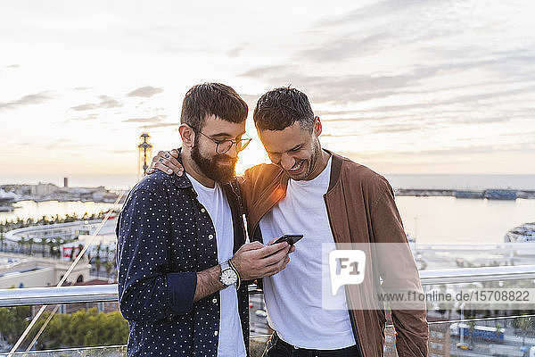 Gay couple using cell phone on lookout above the city with view to the port  Barcelona  Spain