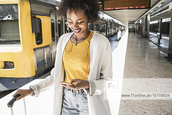 Smiling young woman with earphones and smartphone at platform