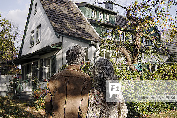 Rückansicht eines älteren Ehepaares im Garten ihres Hauses im Herbst