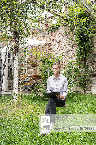 Junge Frau sitzt auf einer Schaukel im Hinterhof und benutzt ein digitales Tablett