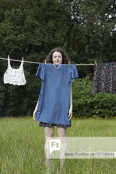 Porträt einer jungen Frau  die hinter einem auf der Wäscheleine trocknenden Kleid steht