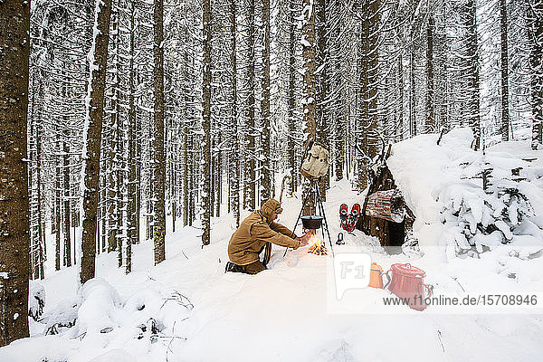 Man preparing tea in winter forest next to a wooden shelter  Salzburg State  Austria