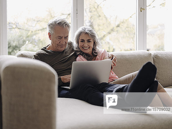 Happy senior couple with laptop relaxing on couch at home