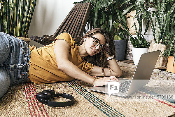 Entspannte junge Frau liegt zu Hause mit Laptop auf dem Boden