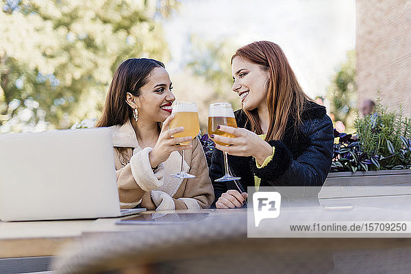 Zwei Freundinnen  die draußen in einem Café mit Biergläsern klimpern