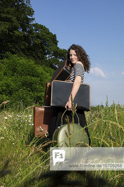 Porträt einer jungen Frau auf einer Wiese mit vielen Koffern