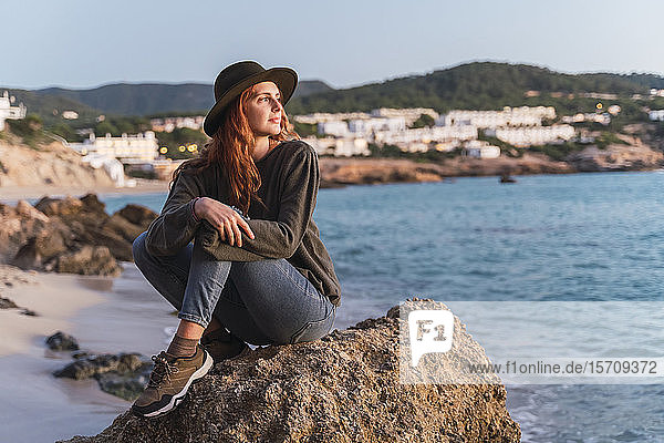 Junge Frau sitzt am Strand und genießt den Sonnenuntergang  Ibiza