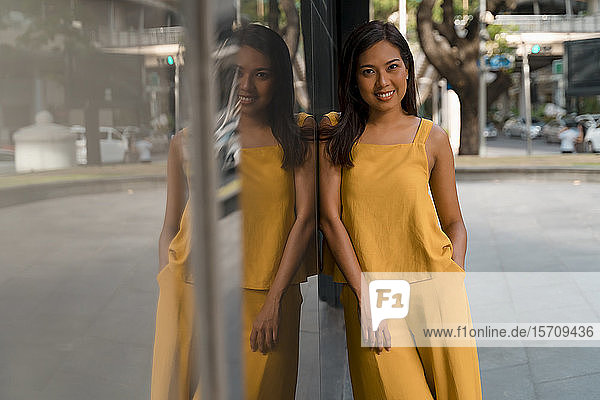 Porträt einer modischen  gelb gekleideten Frau  die an einer Glasfront lehnt