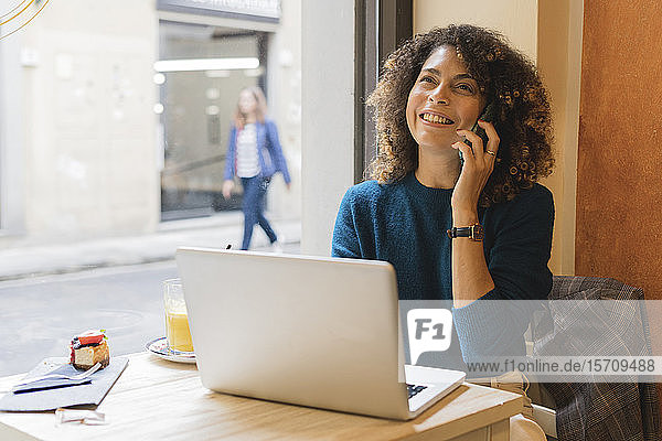 Glückliche Frau mit Smartphone und Laptop in einem Café