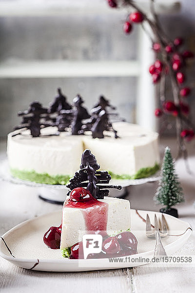 Stück Käsekuchen ohne Backen dekoriert mit Schokoladen-Weihnachtsbäumen auf Teller mit heißer Kirschsauce