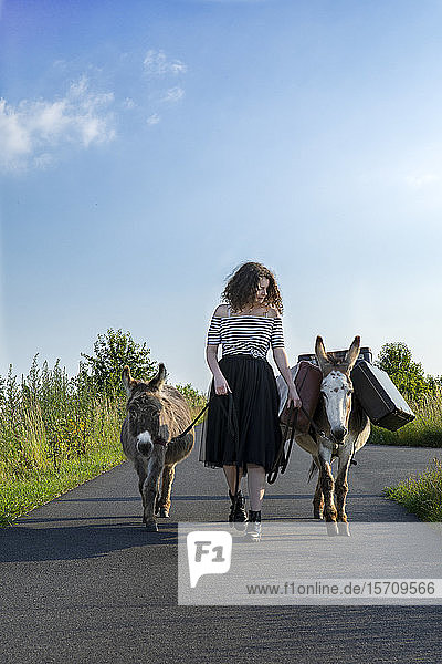 Junge Frau auf Landstraße mit Gepäck tragenden Eseln
