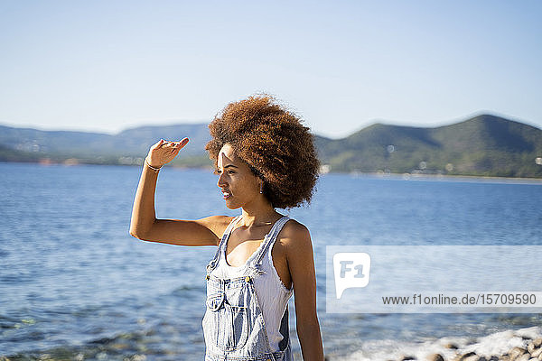 Junge Frau am Strand  die ihre Augen mit der Hand abschirmt