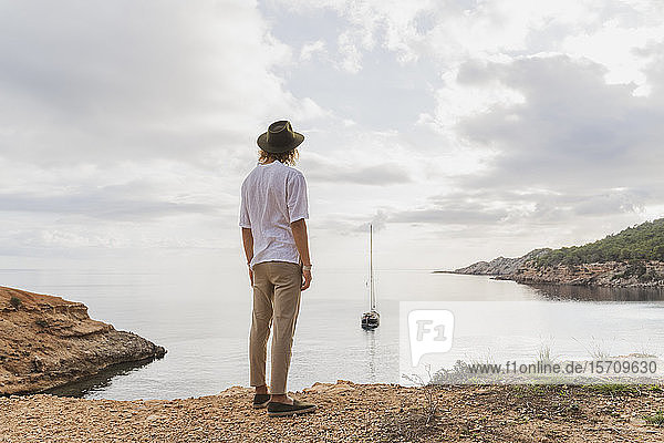 Rückansicht eines jungen Mannes, der vor dem Meer steht und auf das Meer blickt, Ibiza, Balearen, Spanien