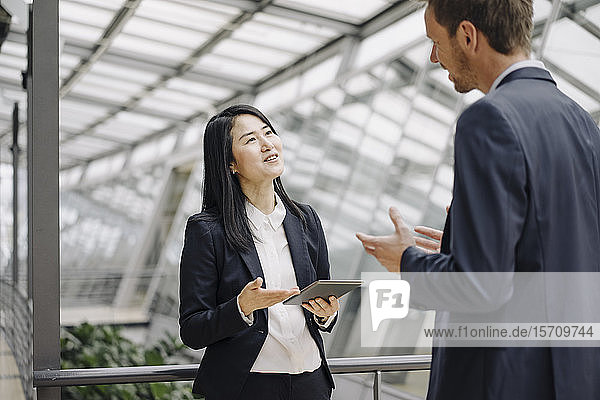 Geschäftsmann und Geschäftsfrau mit Tablett sprechend in modernem Bürogebäude