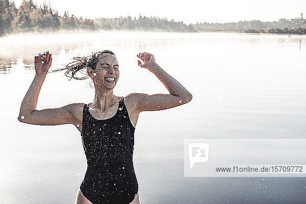 Fröhliche Frau im schwarzen Badeanzug an einem See im Morgennebel
